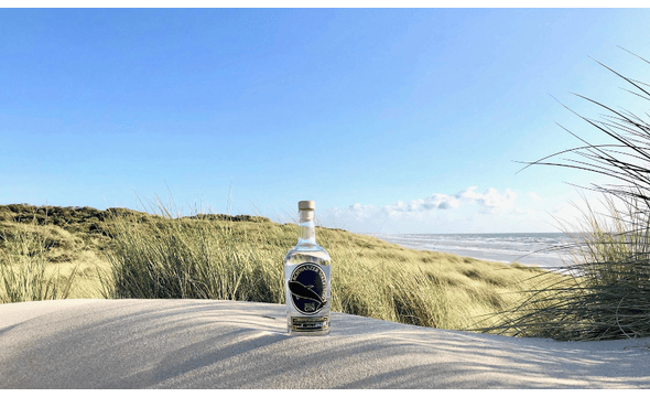 Schwarzer Walfisch Gin am Meer im Sand